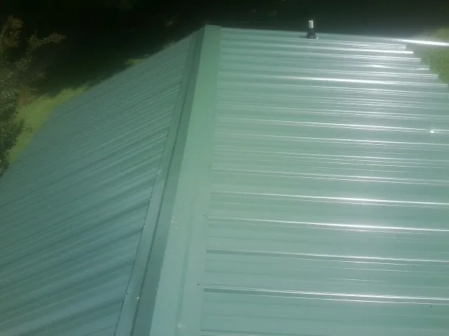 New green metal panels meeting at the ridge of a roof — Flat Roof Repair work by our crew in Genoa